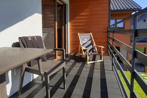 An outdoor balcony with a table and chairs, a wooden chair with a sign, and a metal railing.