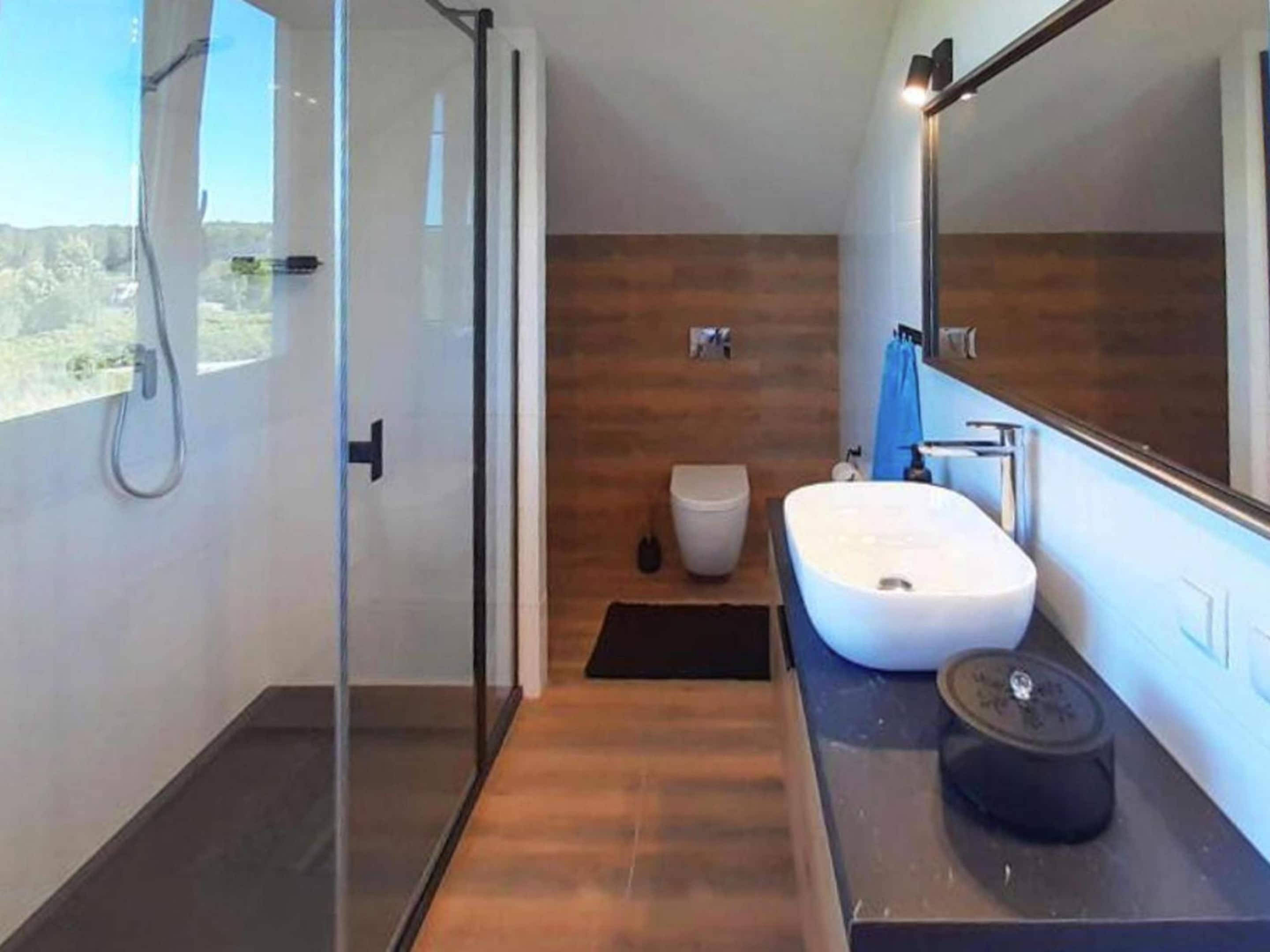 A modern bathroom with a glass shower enclosure, a white sink, and a large mirror.