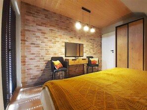 A bedroom with a brick wall, a bed with a yellow bedspread, a desk with a chair, and a television. - 4-bedroom Holiday Home With Sauna and Whirlpool (Mielno)