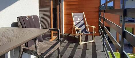 A balcony with a table and chairs, a wooden chair with a sign, and a railing.