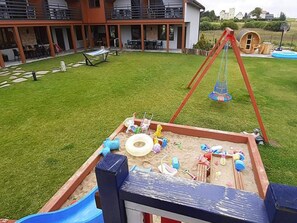 A backyard with a swing set, a sandbox, and a slide. - 4-bedroom Holiday Home With Sauna and Whirlpool (Mielno)