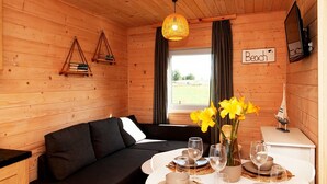 L’intérieur d’un chalet accueillant, avec un canapé noir, une table à manger dressée pour quatre personnes et une fenêtre agrémentée de rideaux.