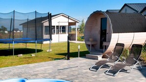 Un jardin avec une piscine, un trampoline, un espace salon extérieur couvert et une maison à l’architecture cylindrique originale.