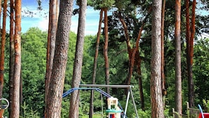 Un parque infantil con un tobogán y columpios, rodeado de árboles altos.