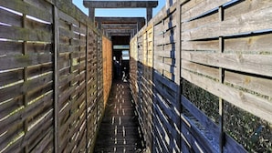 Un estrecho pasillo de madera con suelo de baldosas, bordeado por paredes de madera con listones horizontales.