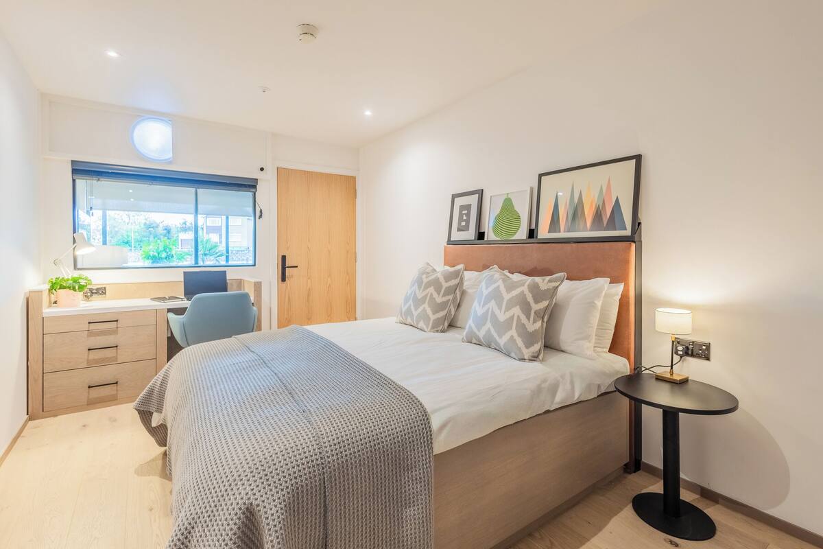 A modern hotel room with a large bed, a desk, and a window with a view of greenery.