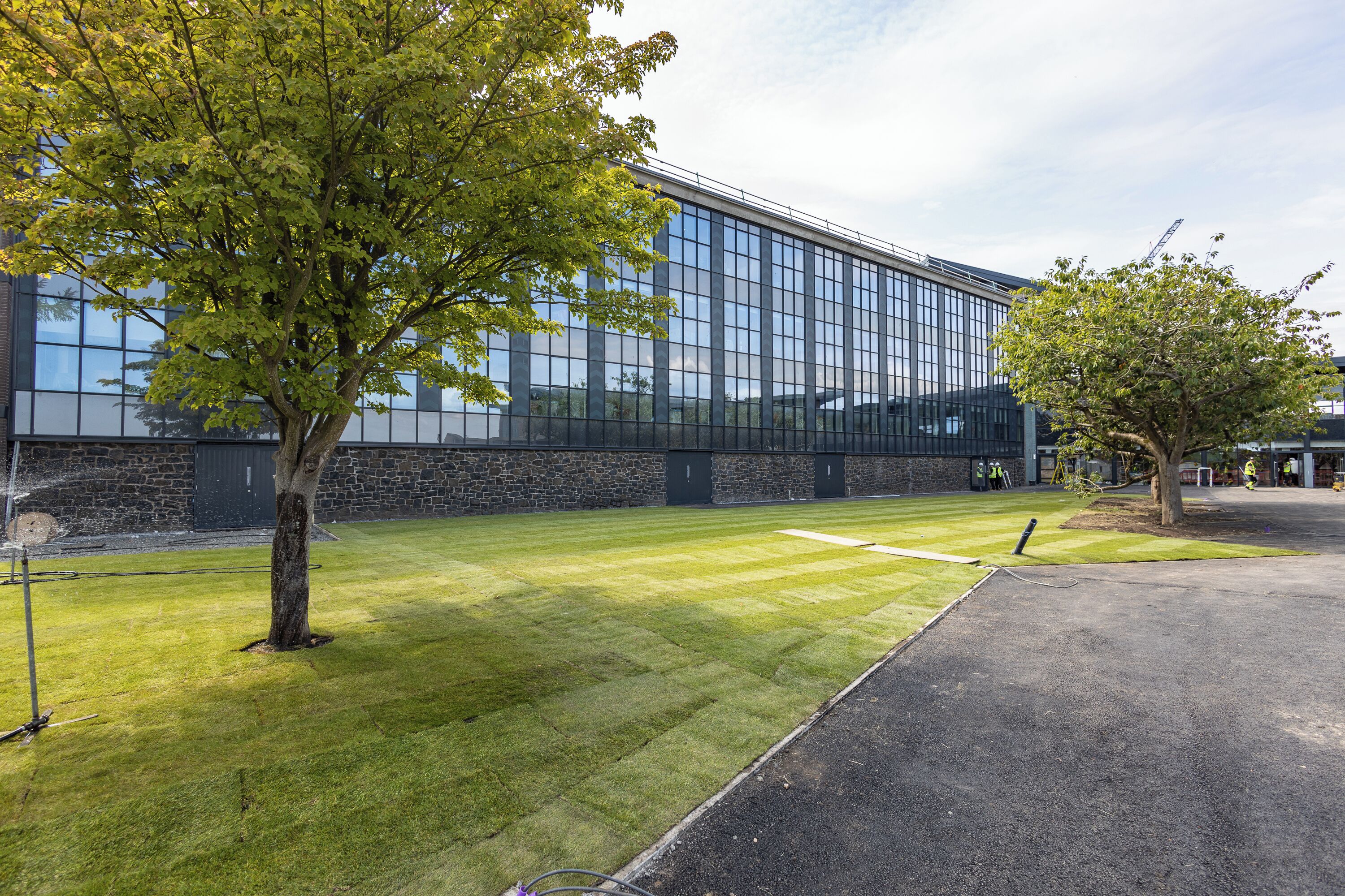 A modern building with a glass facade, a well-maintained lawn, and a paved driveway.