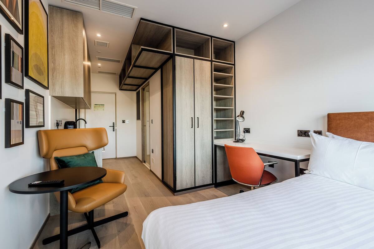 A hotel room with a bed, a desk, a chair, and a wardrobe with multiple compartments.
