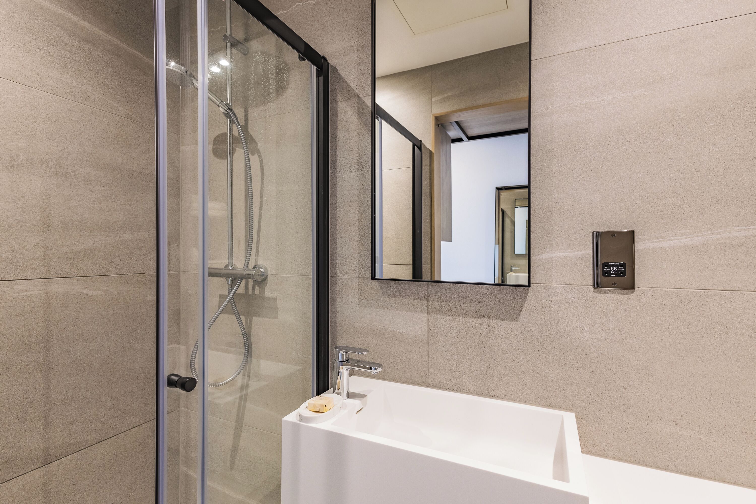 A modern bathroom with a glass-enclosed shower, a white sink, and a mirror on the wall.