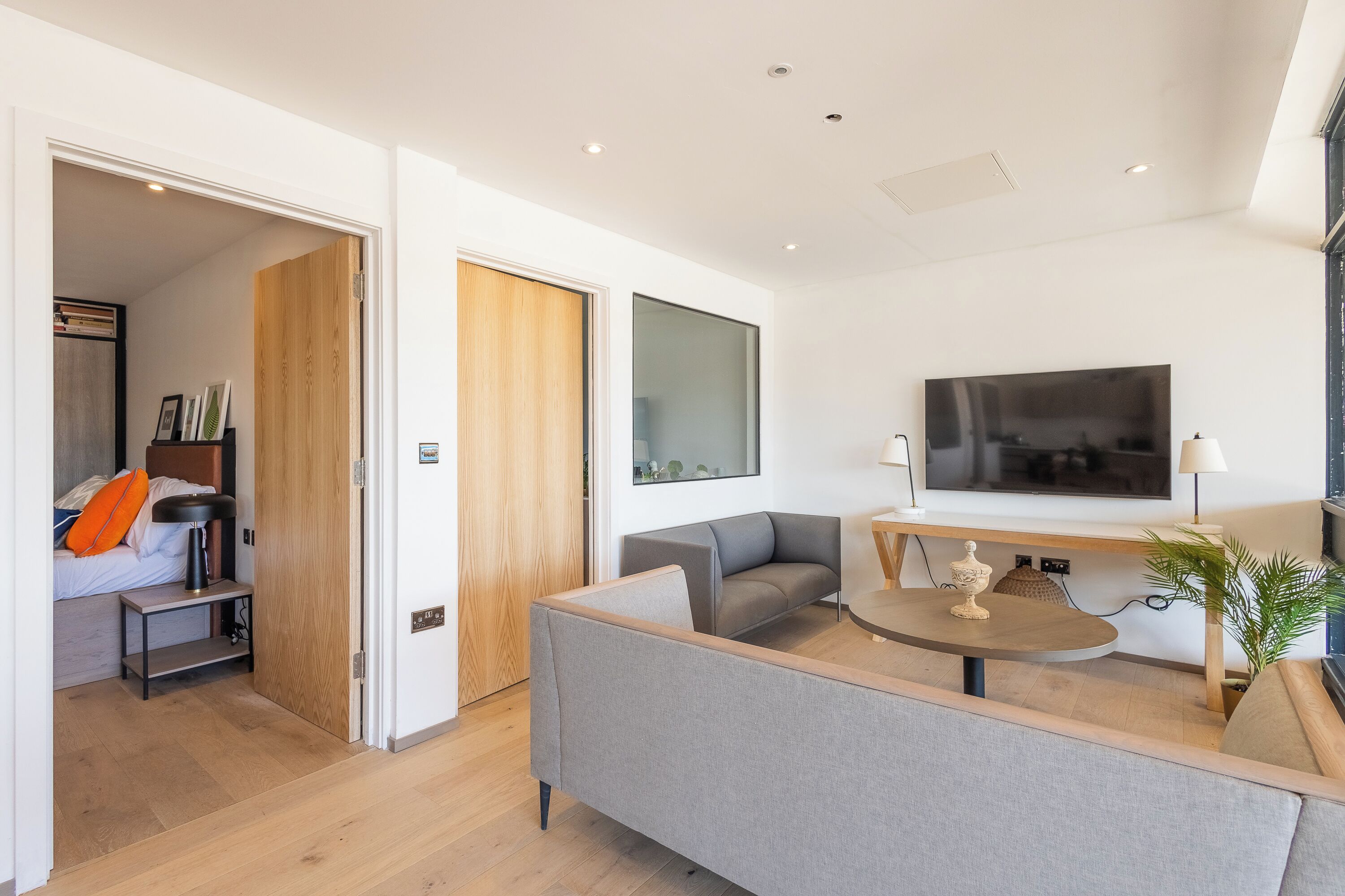 Un salon moderne avec un canapé gris, une table basse en bois et un téléviseur fixé au mur.