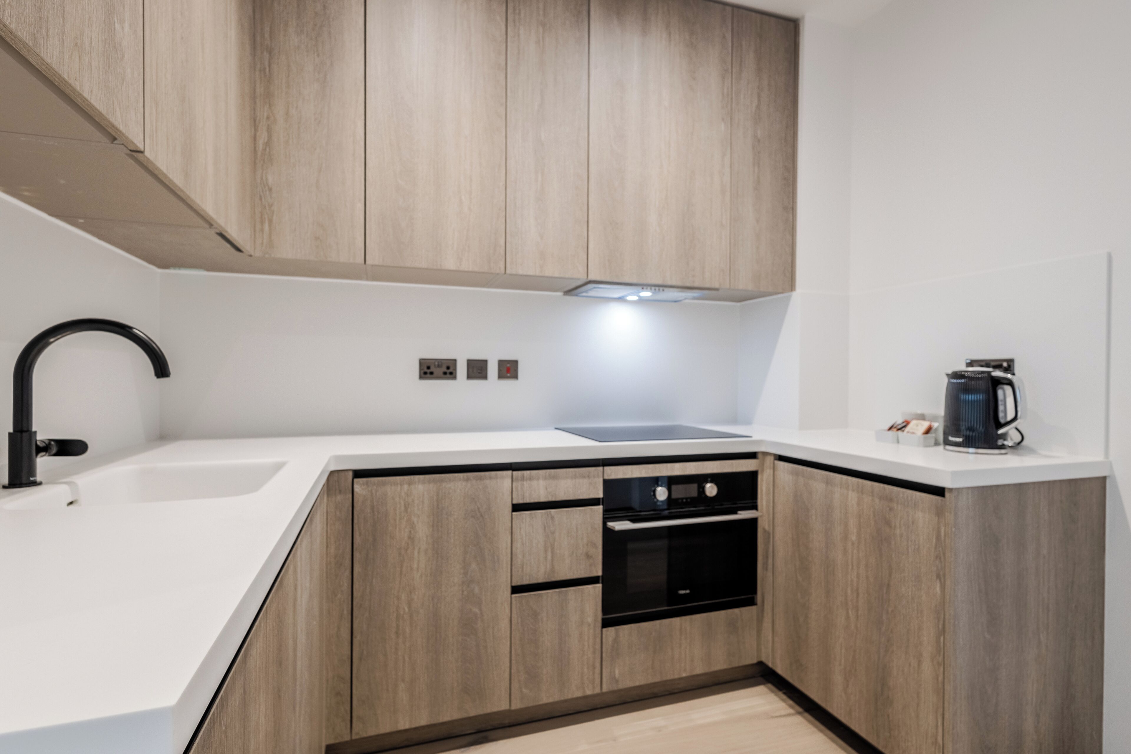 A modern kitchen with wooden cabinets, a black oven, and a coffee maker.