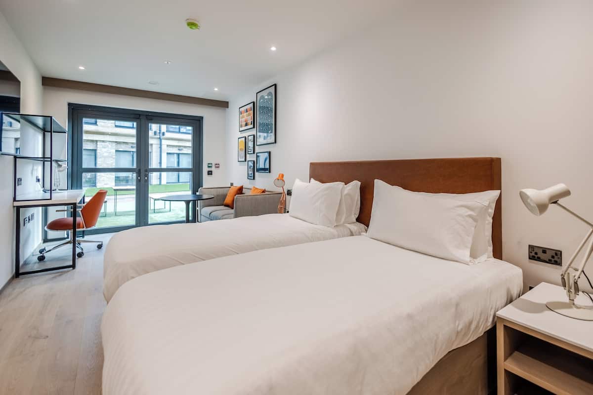 A modern hotel room with two beds, a desk, and a chair.