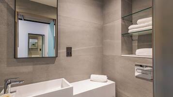 A modern bathroom with a large mirror, a white sink, and a glass shelf with towels.