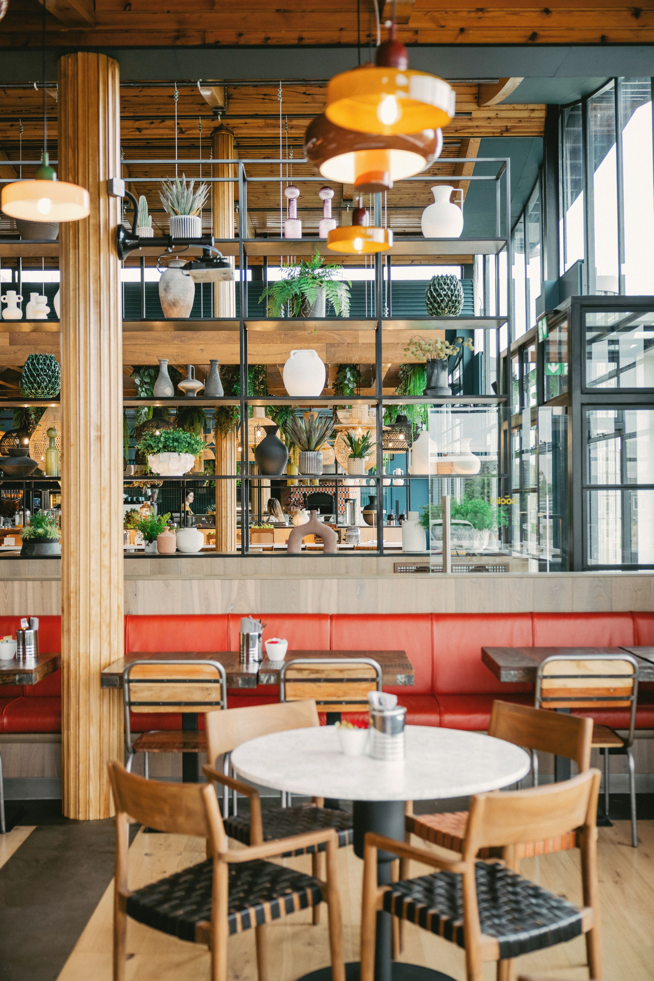 A restaurant interior with wooden beams, shelves with plants, and red booths.