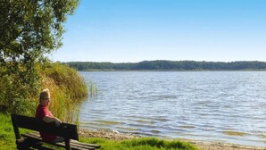 A person sitting on a bench by a lake with a forest in the background. - Ferienhaus Zum Roten Adler in Storkow (Storkow)