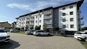 Un immeuble résidentiel à plusieurs étages, doté de balcons, d’une allée pavée et de voitures garées.