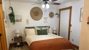 Ein Schlafzimmer mit Bett, Nachttischen, Deckenventilator und dekorativen Wandbildern.