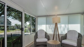 Uma sala de sol com cadeiras de vime, uma mesa de madeira e um abajur.