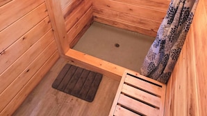 Habitación de cabaña de madera con ventana, zona de ducha y un pequeño banco de madera.