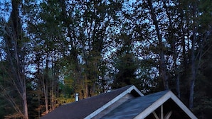 Una cabaña de madera con porche cubierto, cocina al aire libre y zona de estar rodeada de árboles.