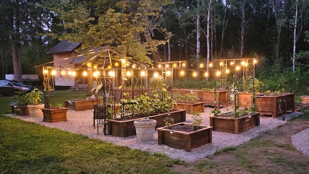 Un jardín con bancales de madera y luces colgantes.