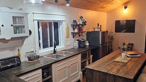 Cocina compacta con horno integrado, un lavamanos y una zona de comedor con mesa de madera.