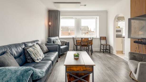 A modern living room with a leather sofa, a wooden coffee table, and a dining area with a wooden table and chairs.