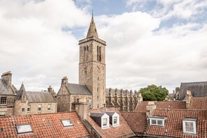 A historic stone tower with a clock, surrounded by traditional buildings with red-tiled roofs. - Muttoes Apartments (No 21) (St Andrews)