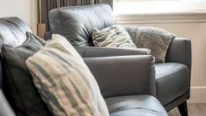 A gray leather sofa with patterned cushions, positioned near a window with curtains.