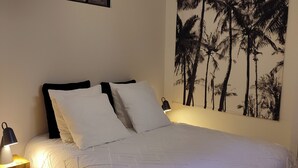 Ein Schlafzimmer mit Bett, Nachttisch, einer Wandlampe und einem großen Gemälde einer tropischen Palme.