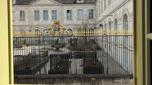 Blick auf ein Gebäude mit Innenhof, mit schwarzem schmiedeeisernen Zaun und aufwendigen Verzierungen sowie einer zentralen Fontäne.