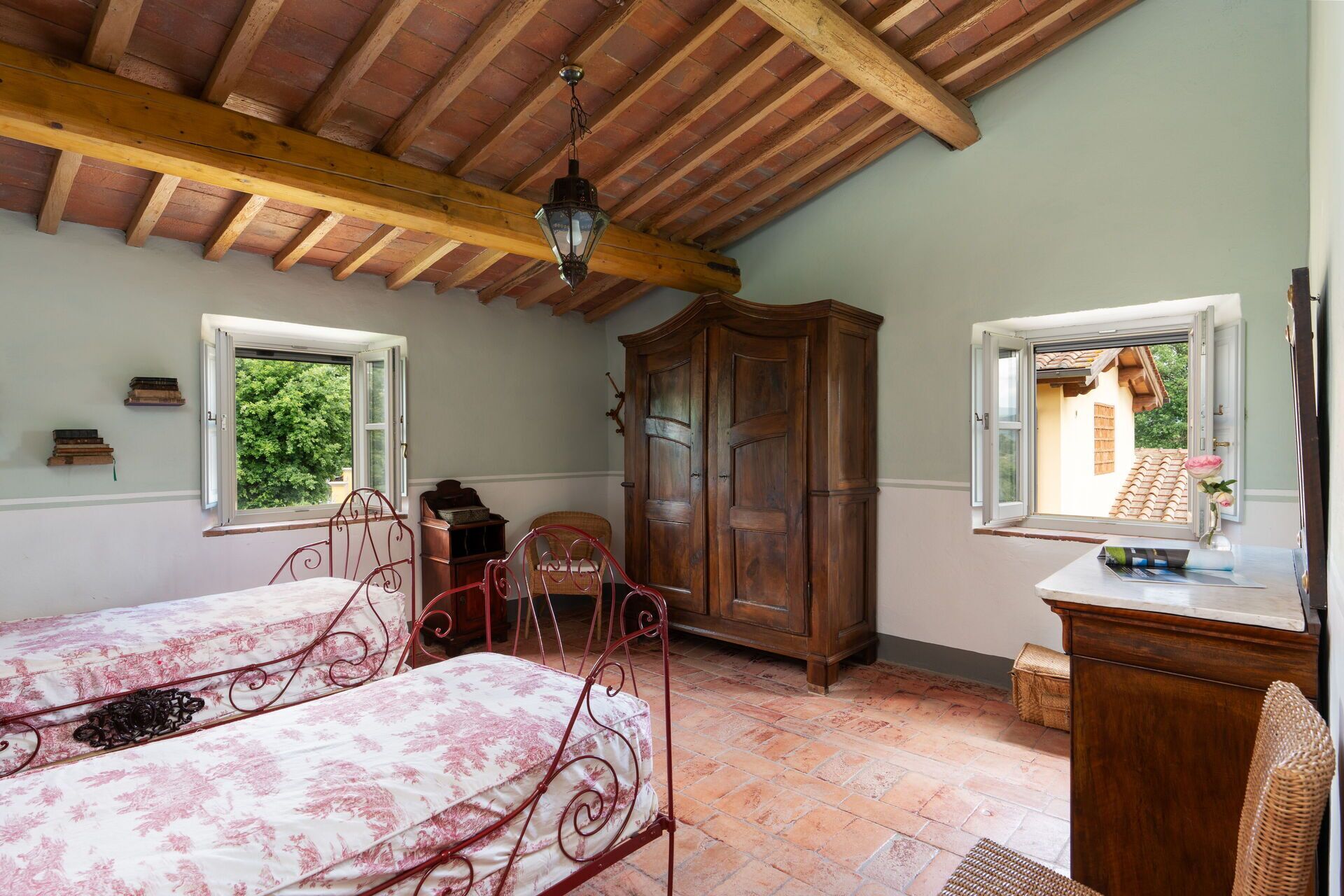 Une chambre avec deux lits, une armoire en bois et une fenêtre donnant sur une maison.