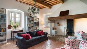 Una sala de estar acogedora con un sofá negro, sillones estampados, chimenea, estanterías y techo de madera.