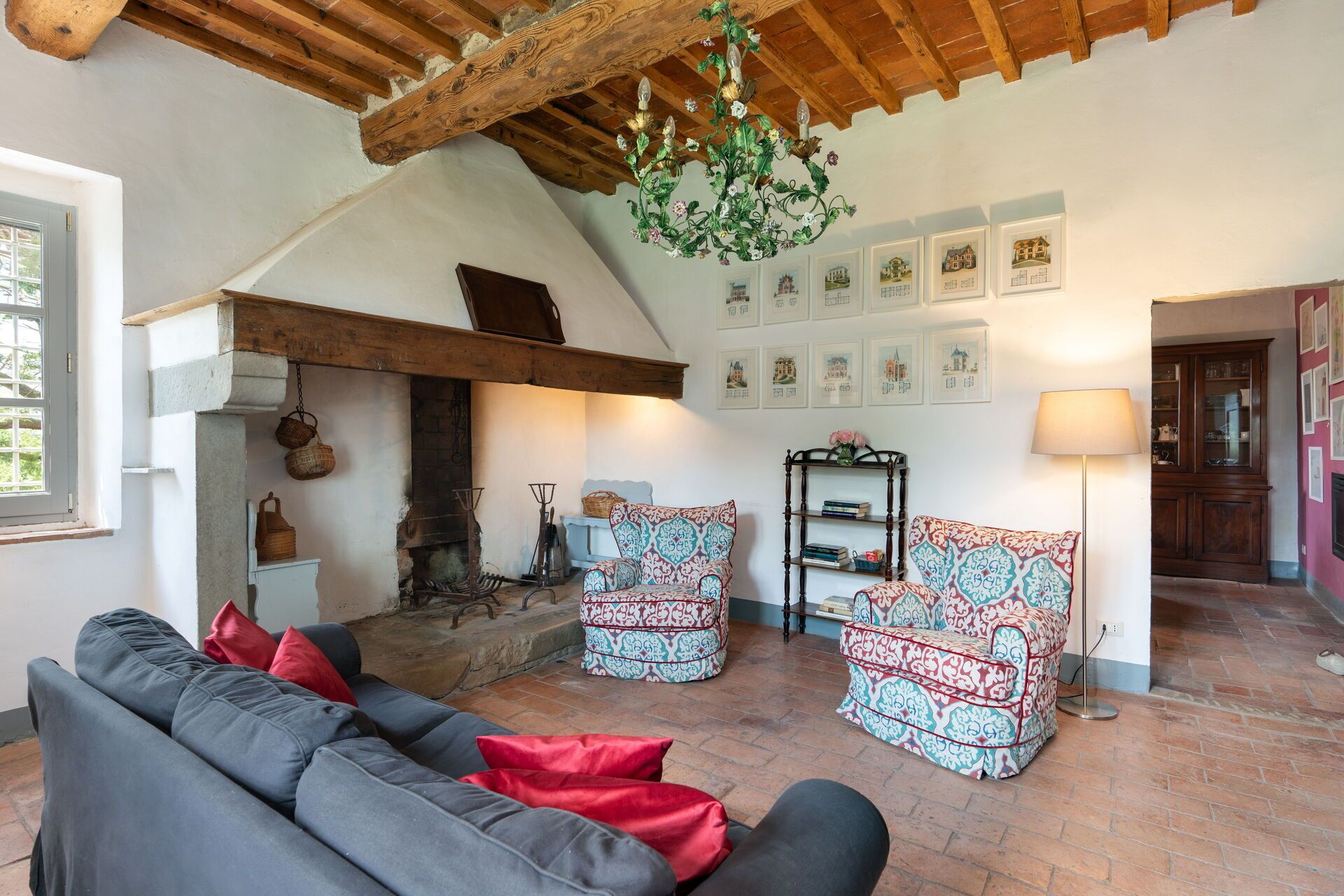 A cozy living room with a fireplace, a sofa, patterned armchairs, and a chandelier.