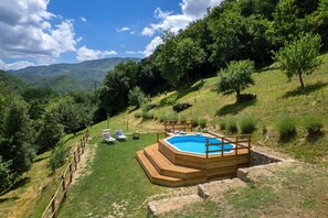 Un jacuzzi rodeado por una terraza de madera, con un área de césped y sillones de descanso.