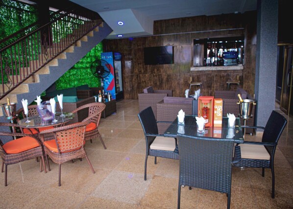 A lobby with a staircase, wicker furniture, a bar area, and a television screen. - Prince Xclusive Royale Hotels (Awka)