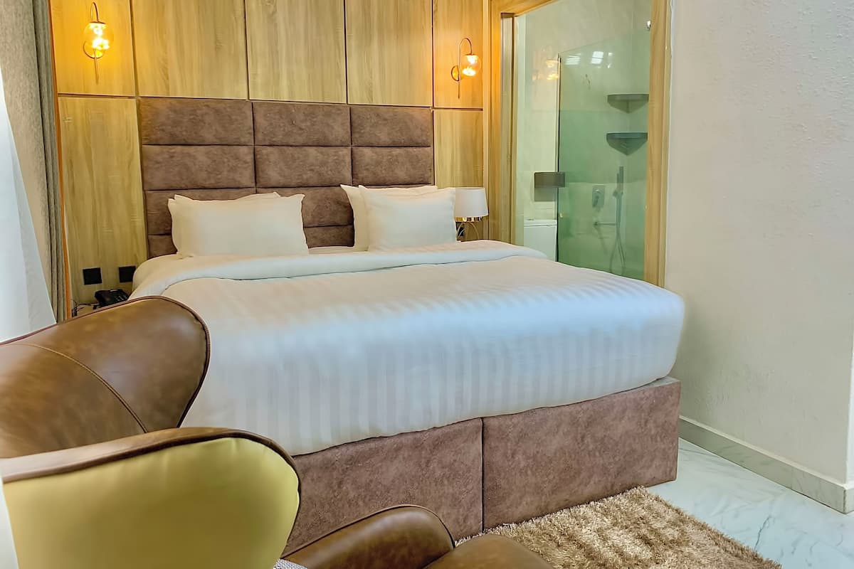A modern hotel room with a large bed, a wooden headboard, and a glass shower enclosure.