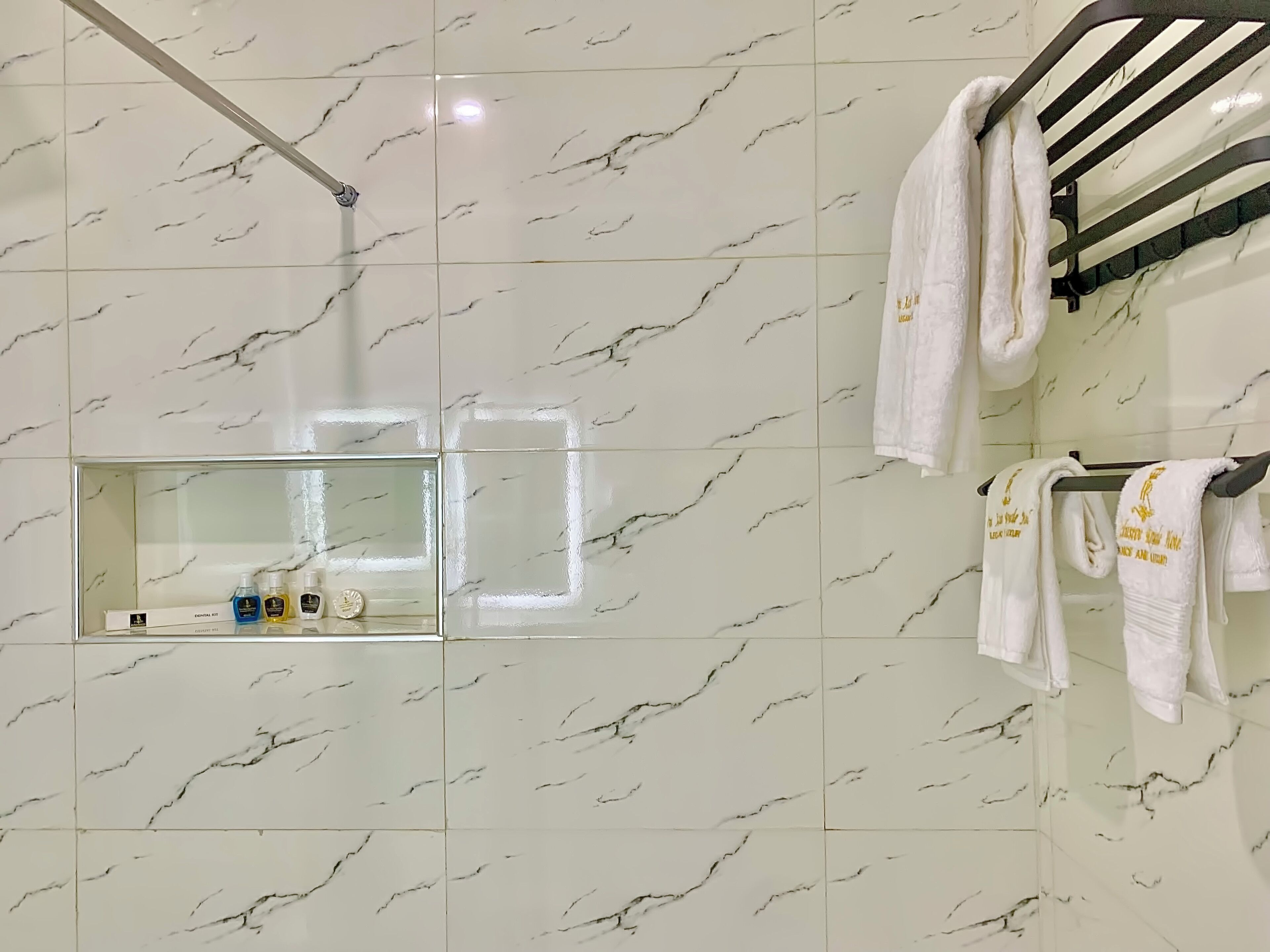 Een badkamer met witte marmeren tegels, een wastafel met glazen ombouw en witte handdoeken met gouden tekst.