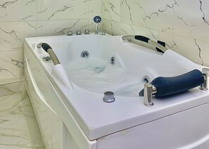 Une baignoire blanche, dotée de plusieurs robinets et d’une molette de réglage, placée devant un mur recouvert de carreaux de marbre.
