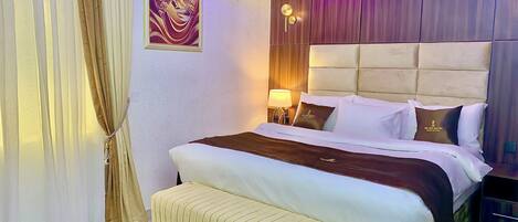 A hotel room with a bed, a headboard, a bedside table with a lamp, and a wall-mounted air conditioner.