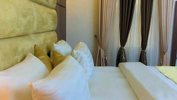 Quarto de hotel com uma cama grande, várias almofadas, uma luminária fixada na parede e uma janela com cortinas.