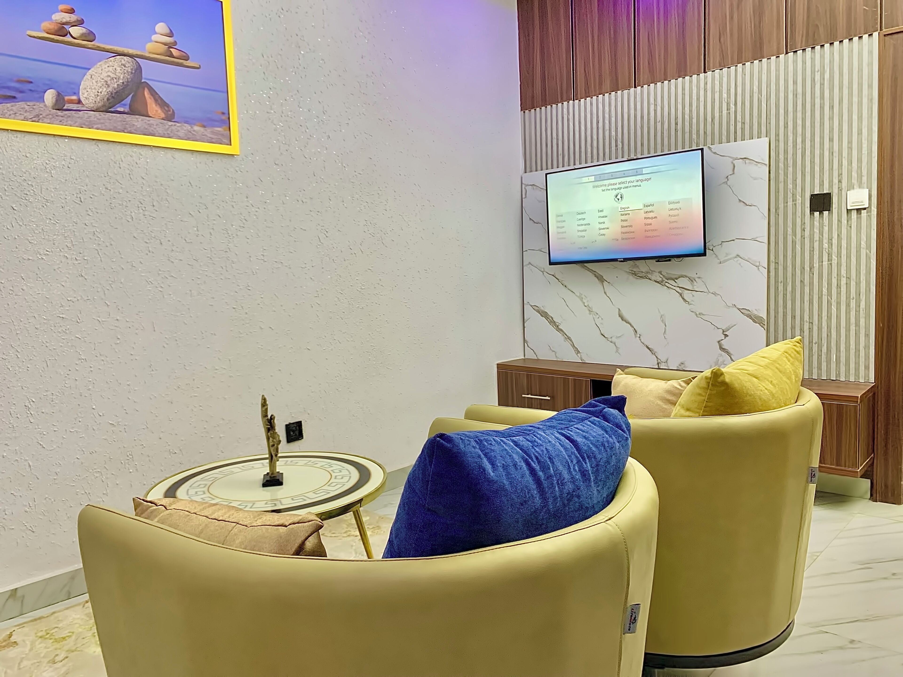 Una sala de estar moderna con una pared de mármol, un televisor montado y dos sillones de cuero con cojines.