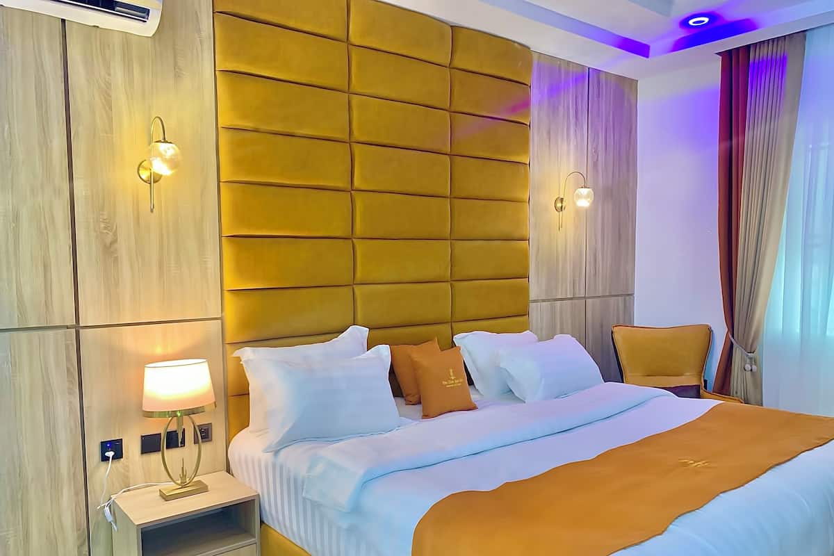 A hotel room with a large bed, a bedside table, a lamp, and a wall-mounted light fixture.