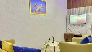 Un salon moderne avec des canapés jaunes, une petite table ronde et un téléviseur fixé au mur.