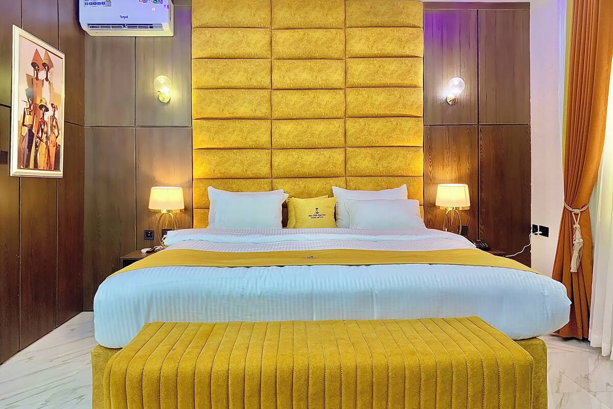 A hotel room with a large bed, two bedside tables, a wall-mounted air conditioner, and a framed picture on the wall.