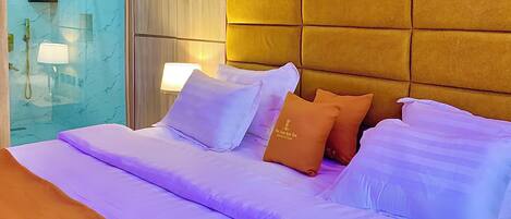 A hotel room with a bed, a headboard, and a wall-mounted lamp.