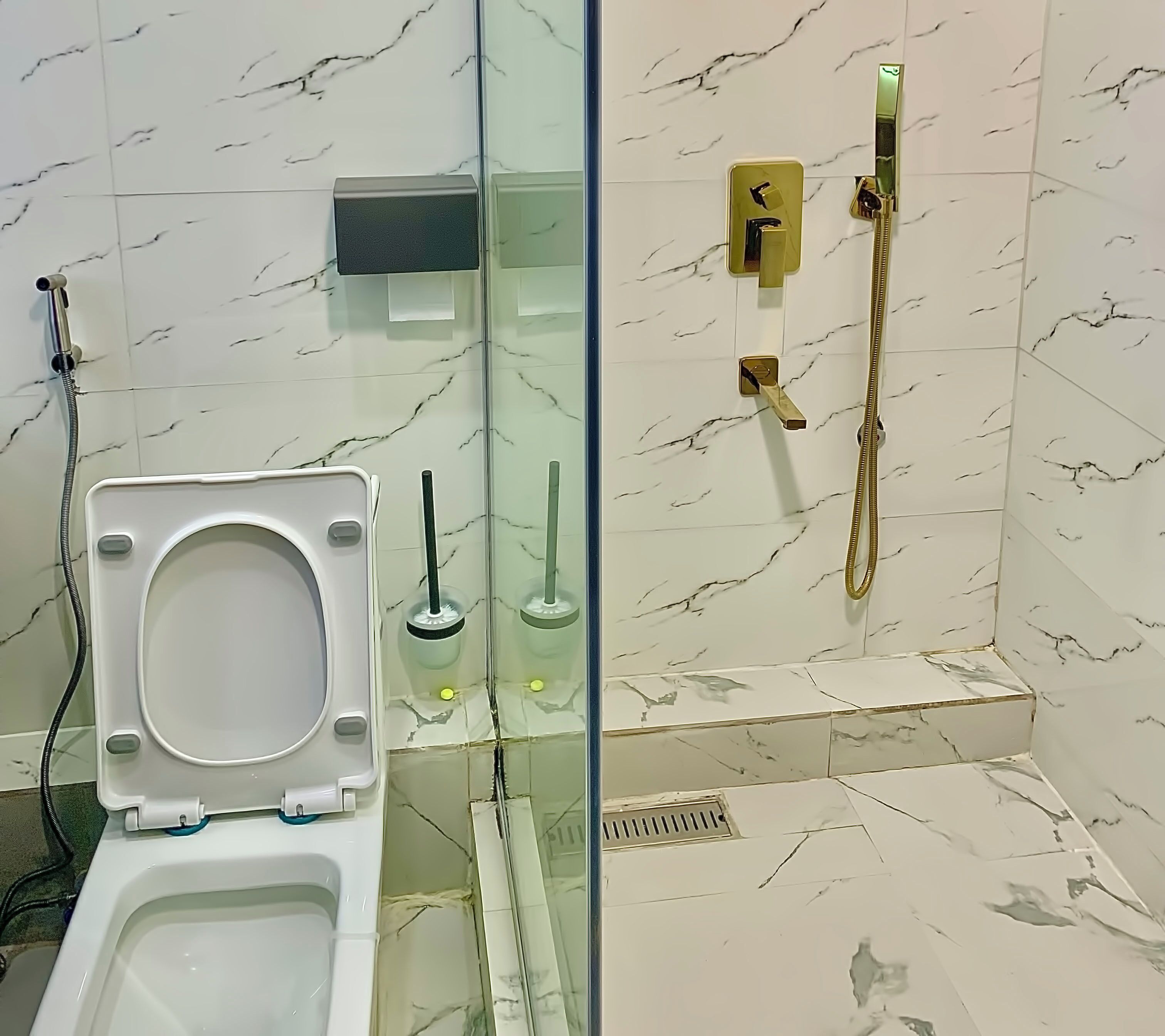 A bathroom with a toilet, a glass-enclosed shower, and marble-tiled walls.
