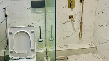 A bathroom with a toilet, a glass-enclosed shower, and marble-tiled walls.