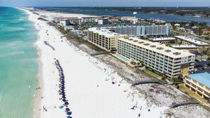 Een kusthotel met meerdere gebouwen, een lang strand met parasols en een helder uitzicht op de oceaan.