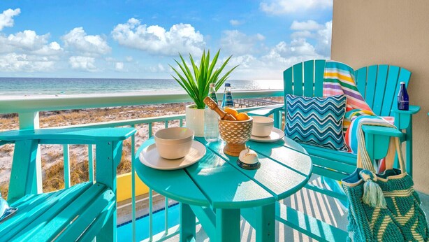 Een turquoise terras met een tafel voor twee, uitkijkend op een strand.